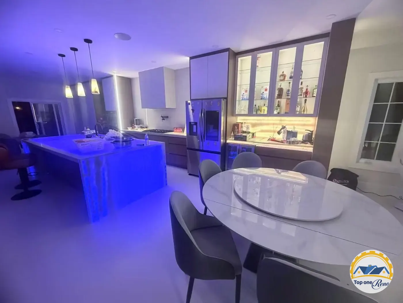 Completed custom kitchen with blue LED-lit island, glass display cabinetry, and dining table by Top One Reno
